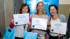 Three women hold certificates to the camera