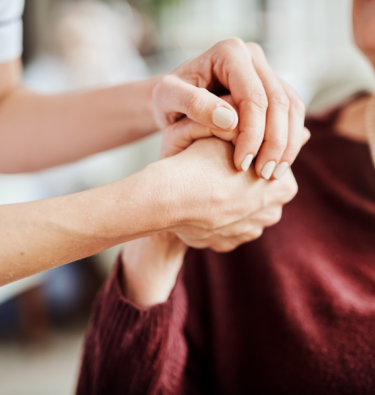 Shows elderly woman holding hands with carer