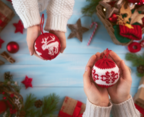 Shows two pairs of hands holding Christmas decorations