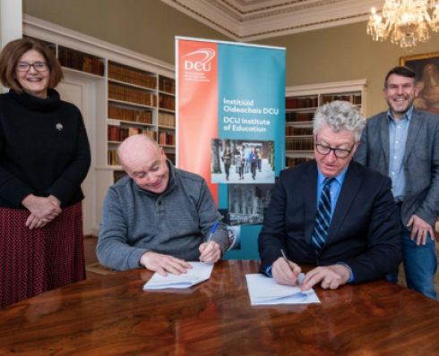 Two people signing and agreement with two others smiling 