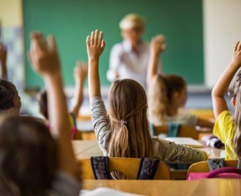 Shows classroom with children raising their hands