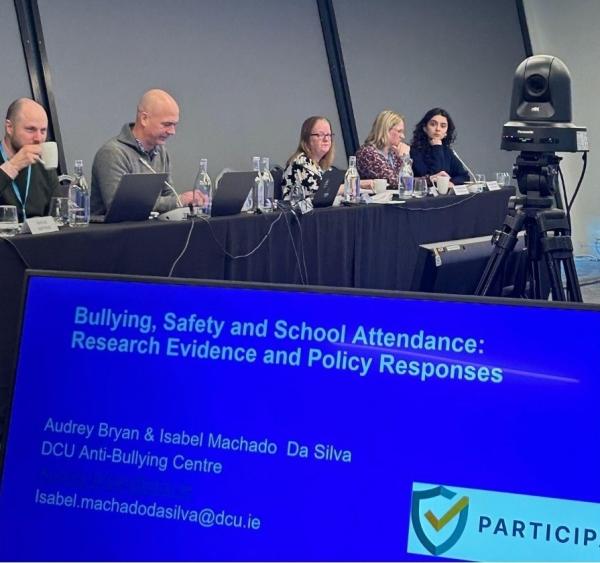 Researchers on a panel with a laptop reading the title of the presentation 