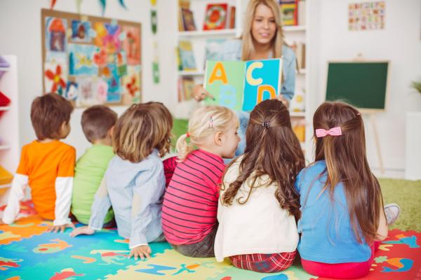 A group of young children listening to their playschool teacher.