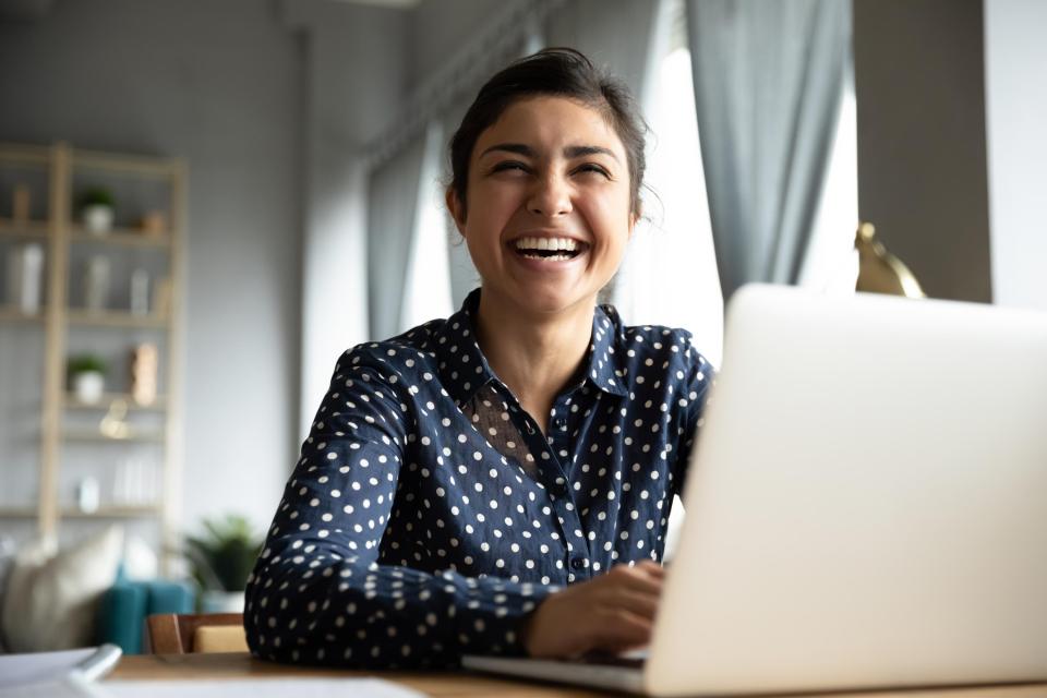 A woman sitting in front of a laptop laughing to the camera.