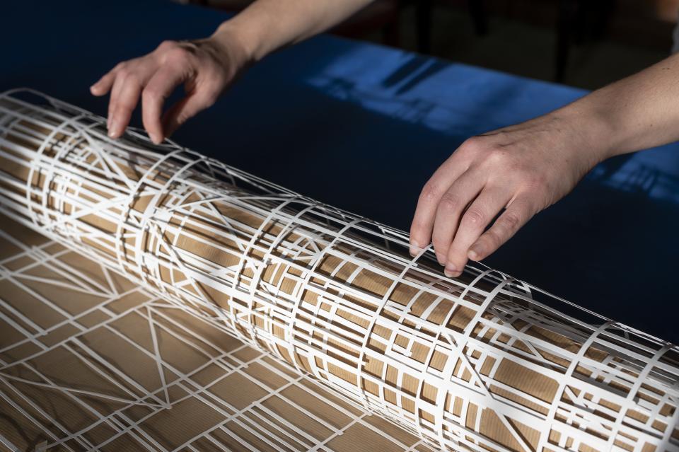 Image of hands touching laser cut paper rolled up on a wooden table