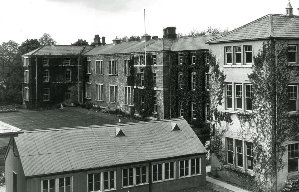 Black and white photo of Albert College, DCU - a large old bricked building covered in ivy 