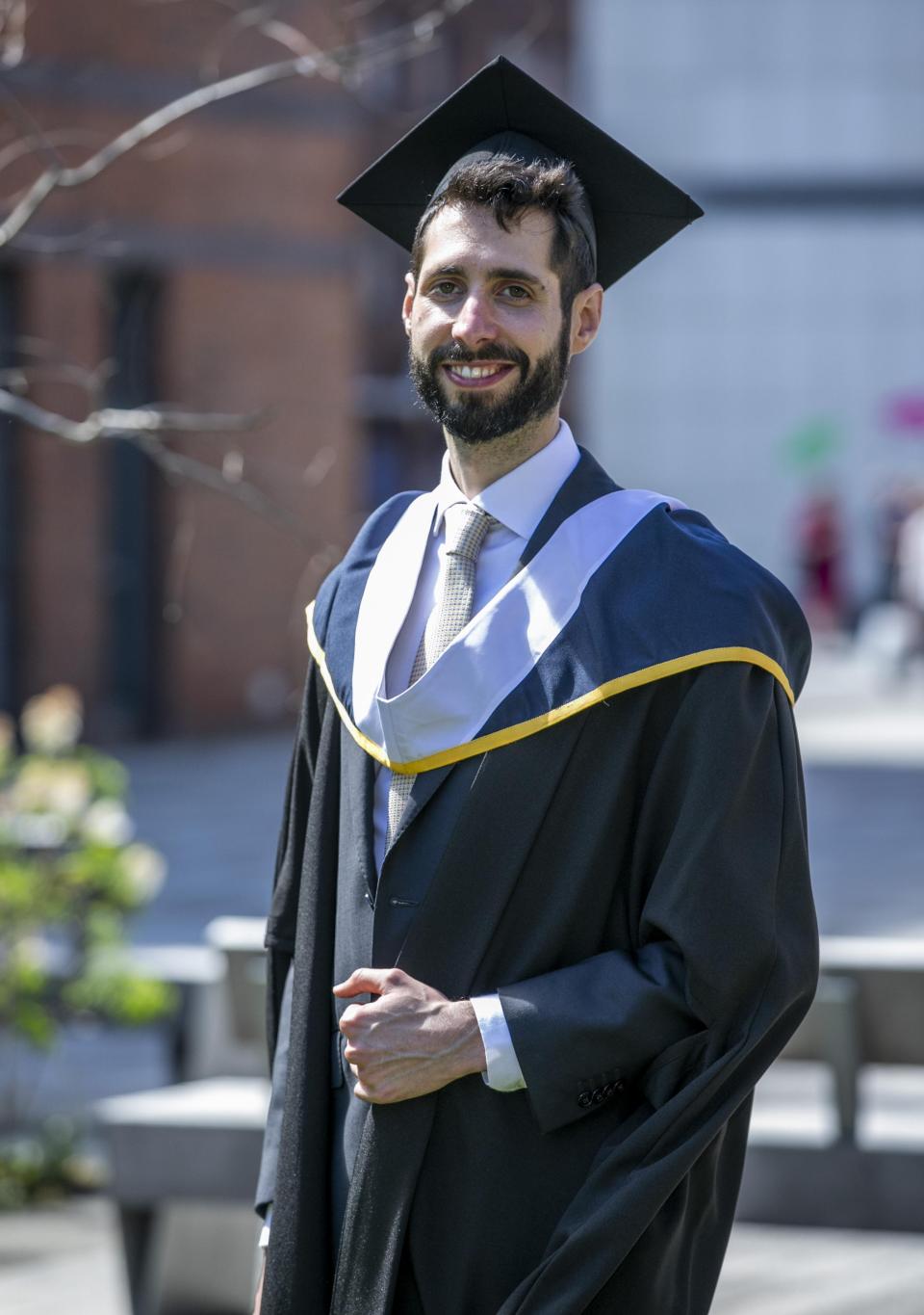 Héctor Muiños, a Spanish gradate in MA Creative Writing, poses for the camera in his graduation cap and gown.