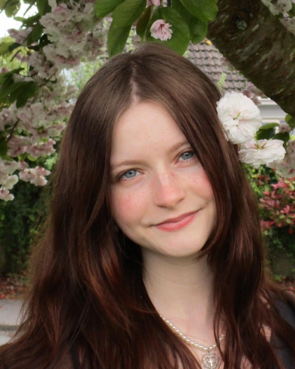 woman with brown hair in a black jacket against green trees in the background