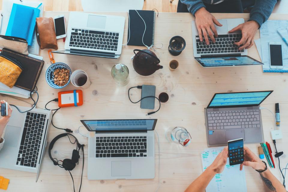 Arial shot of hands working with laptops at a wooden table with smartphones and notebooks.