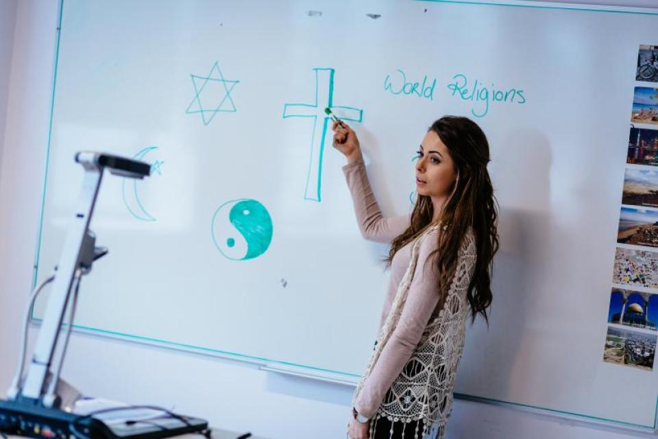 Student standing at a white board teaching a class