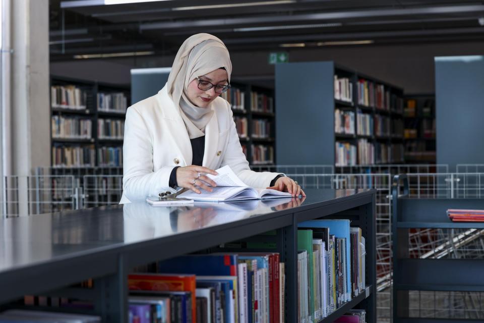 student standing at low bookshelf turning pages in a book