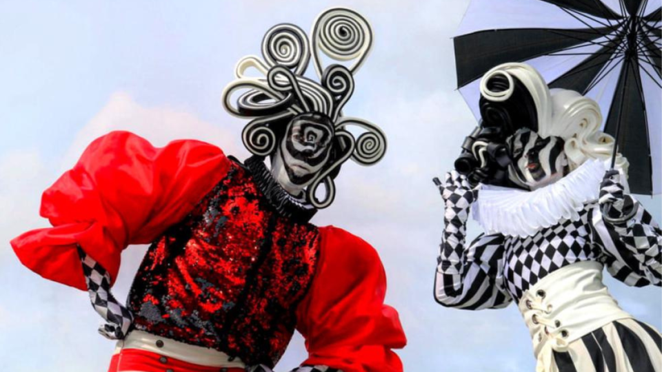 Street performers on stilts wearing red and white with black stripes