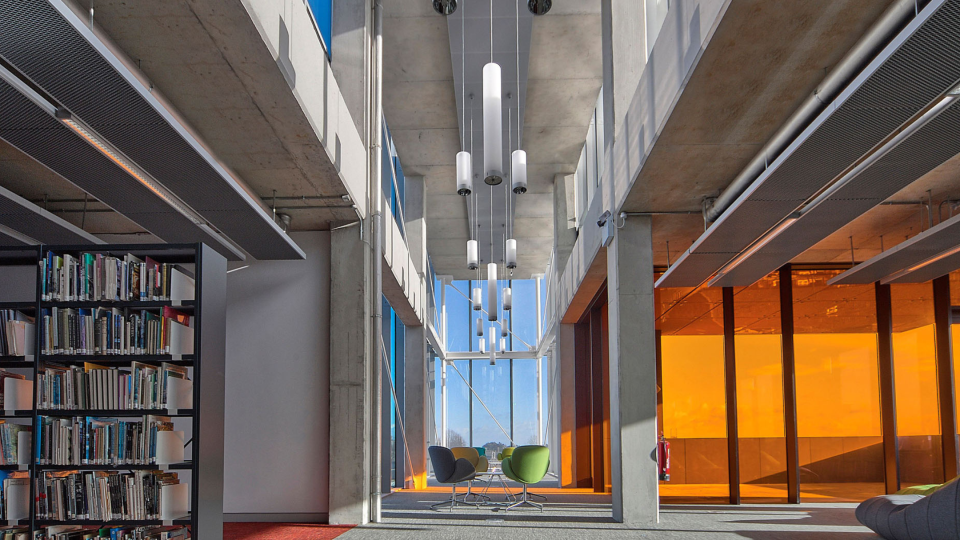 Inside Cregan Library building with books on the left side of the image and orange windows on the right 