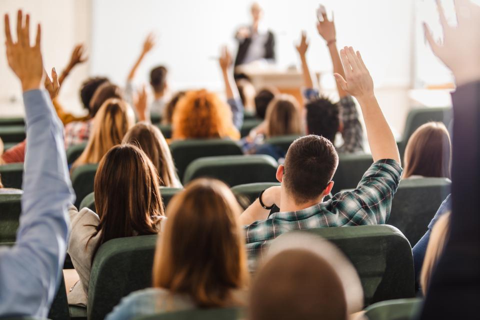 A group of colleagues in a lecture hall with their hands raised, viewed from behind. 