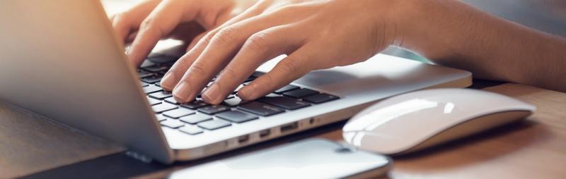 Hands typing on laptop, with mouse and mobile on desk