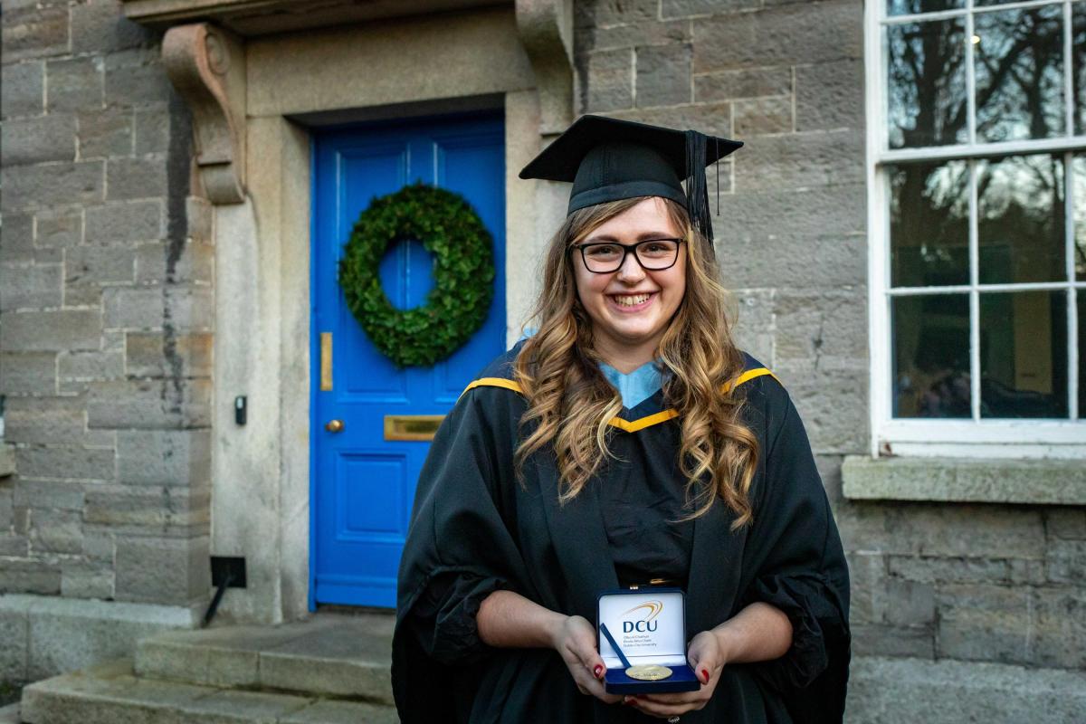 student holding medal in graduation gown
