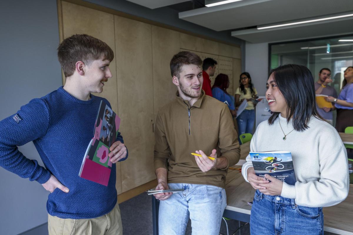 Mixed group of 3 students chatting with materials in hand