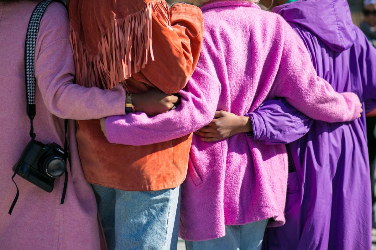 Four women dressed in pinks and purples hugging