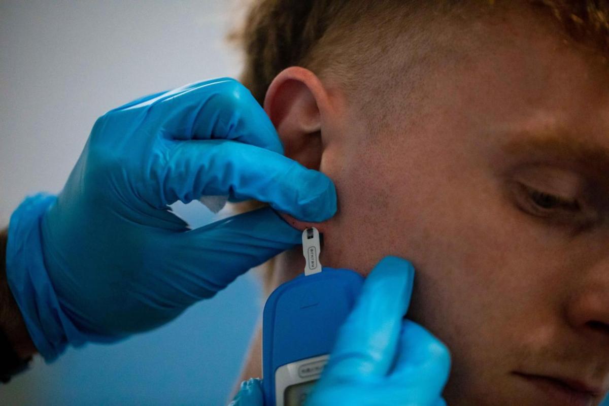 hands in rubber gloves touching a persons ear with medical equipment