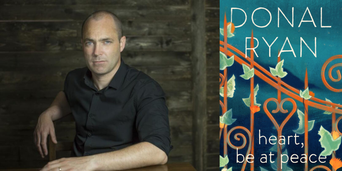 Author Dolan Ryan, man with shaved head sits at a table with a black background. 