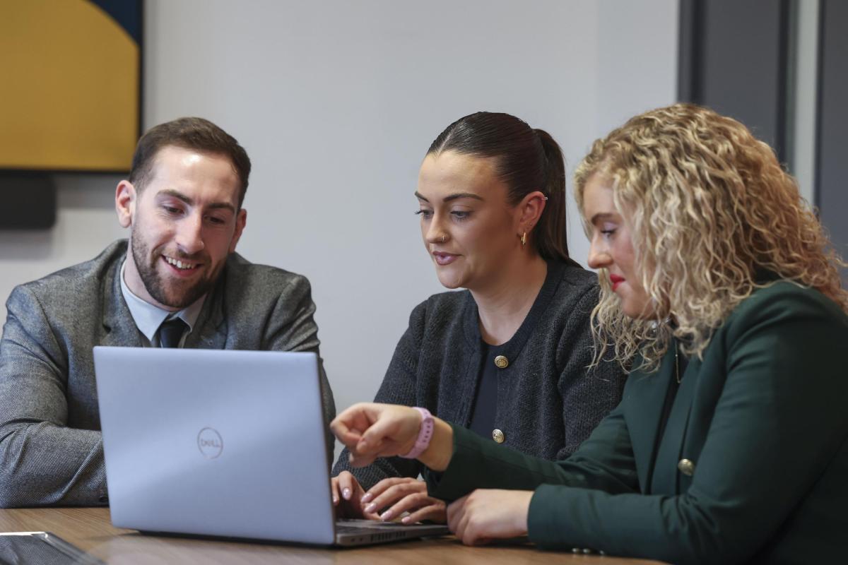 Three colleagues working collaboratively at a laptop.