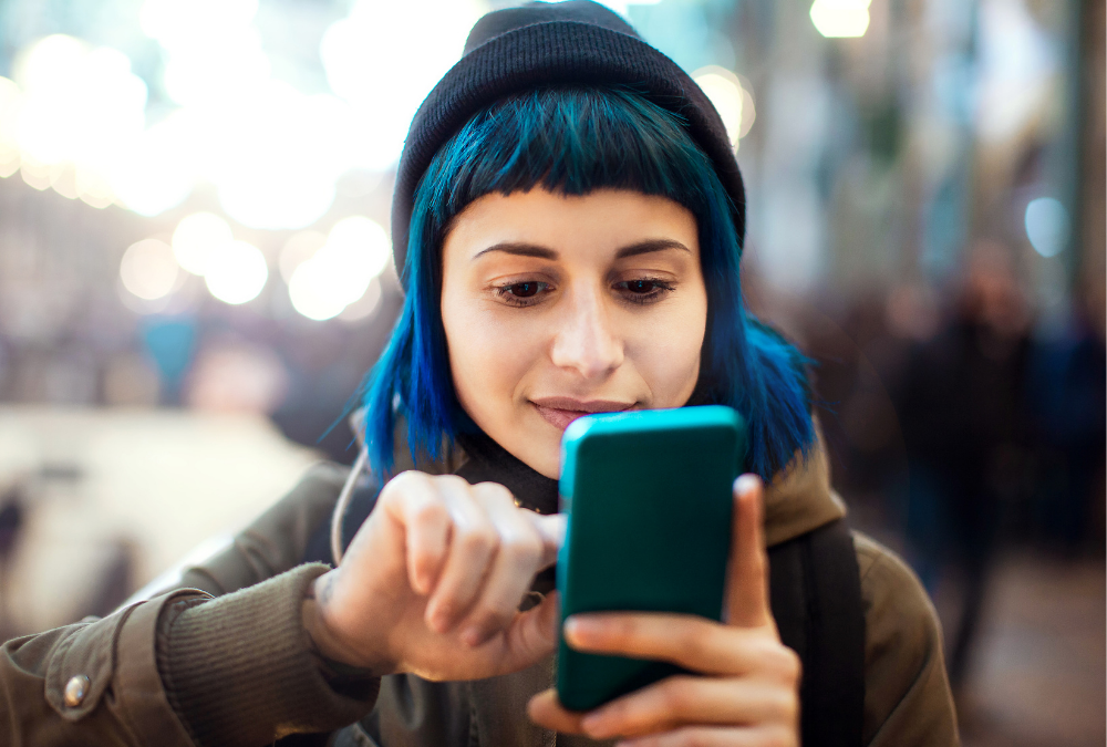 Girl with hat and blue hair reading her phone