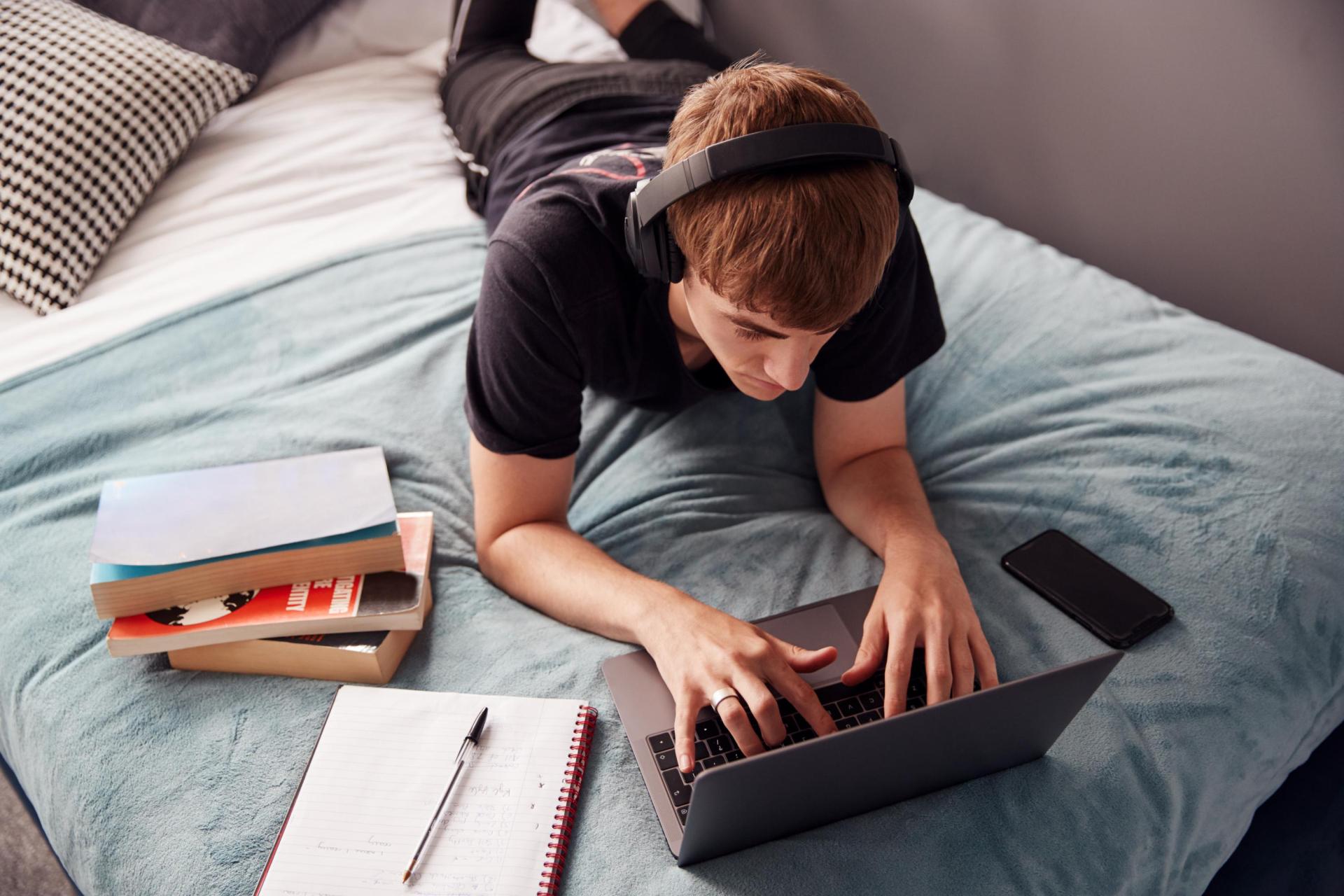 Male student lying on the bed at his laptop