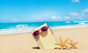 A beach with a book with sunglasses on it stuck in the sand, beside two starfish