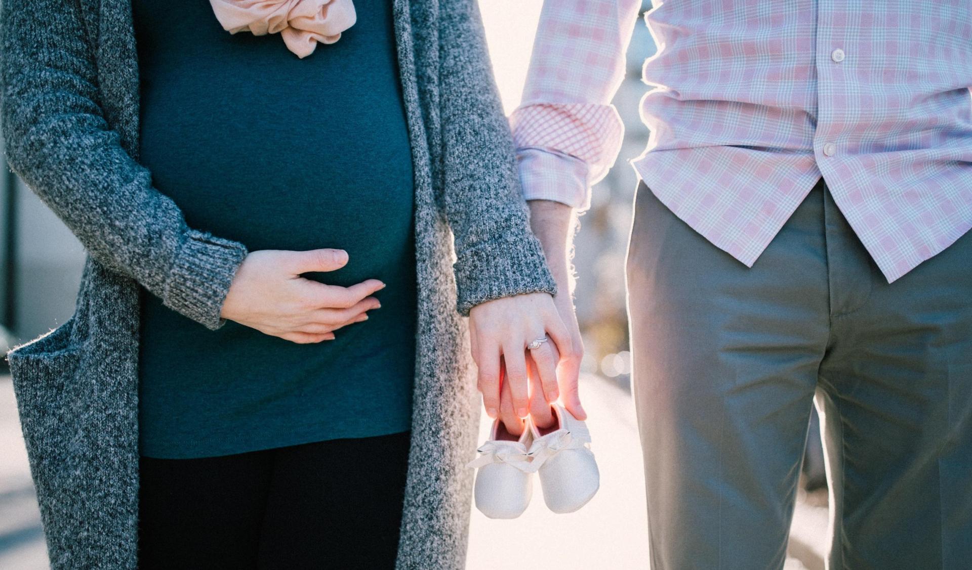 Man and Pregnant Woman holding hands with 2 baby shoes in their hands