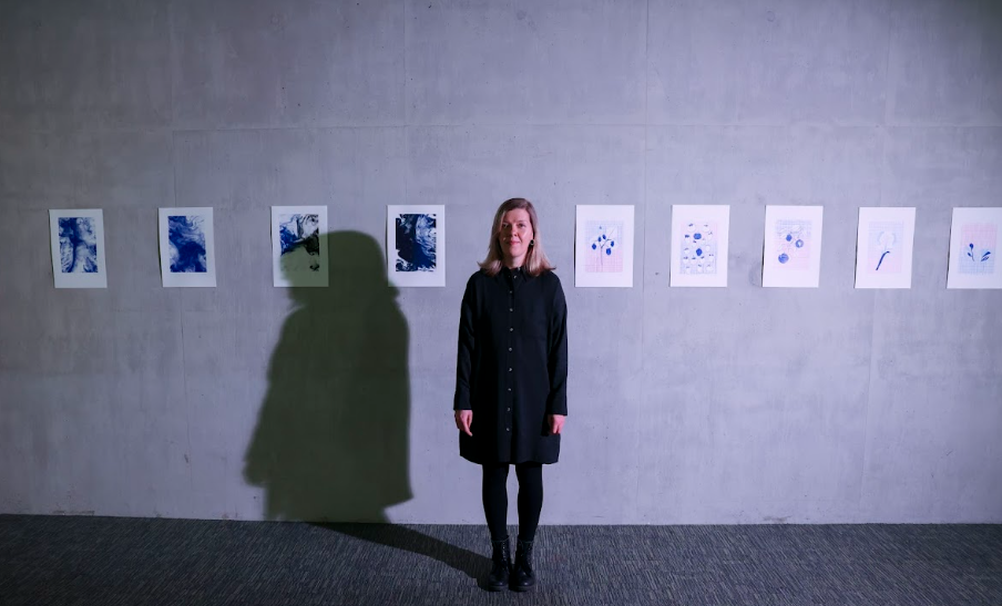 Women in black dress stands in front of concrete wall with artwork displayed 