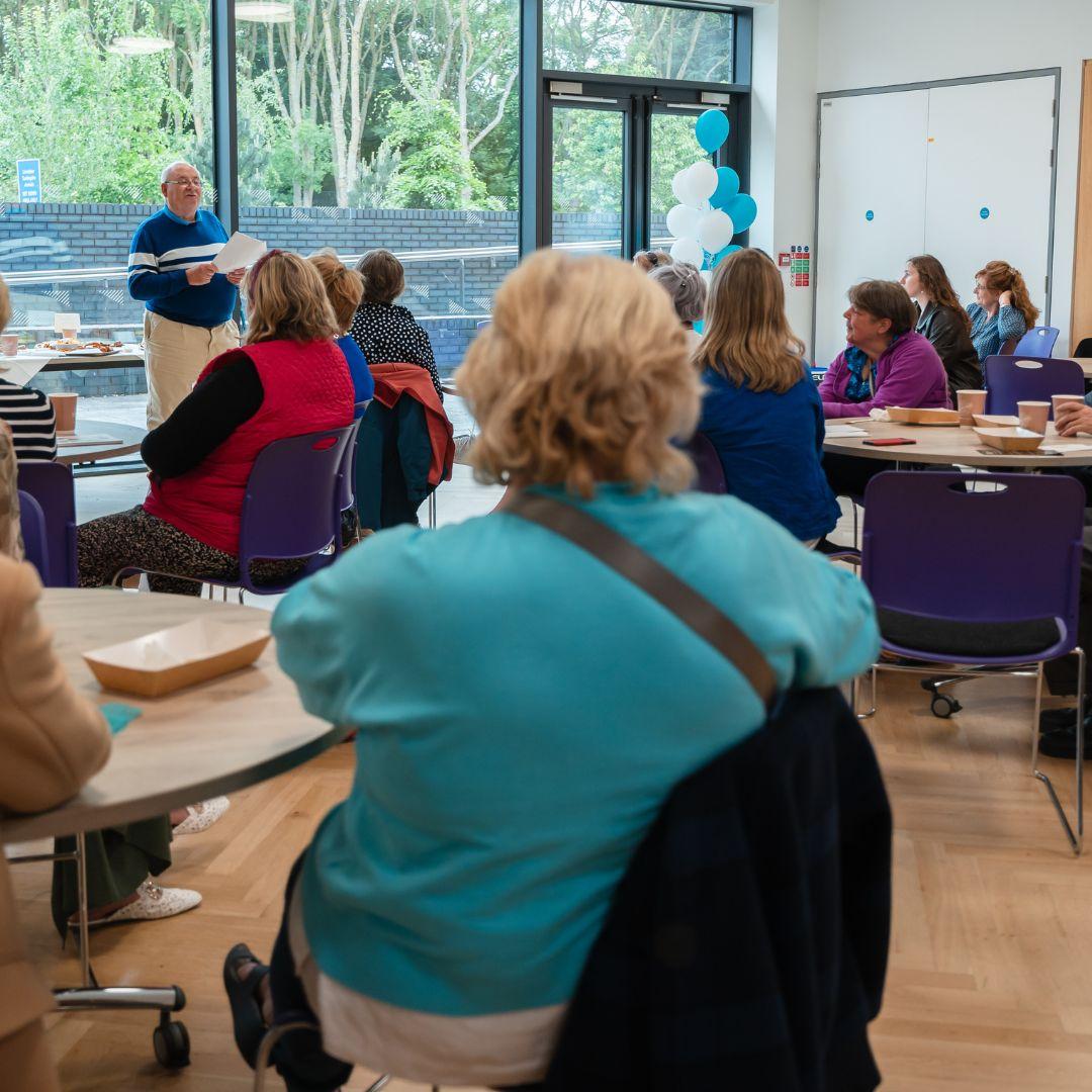 Group of people sitting in a room listening to a person reading