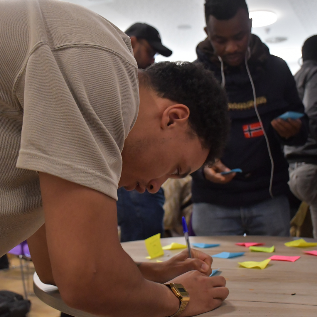 Man leaning down to write on multi coloured paper